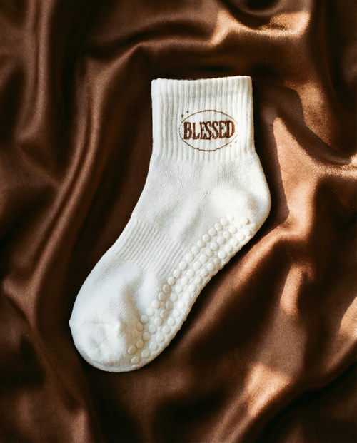 White grip sock with 'Blessed' text on a brown fabric background