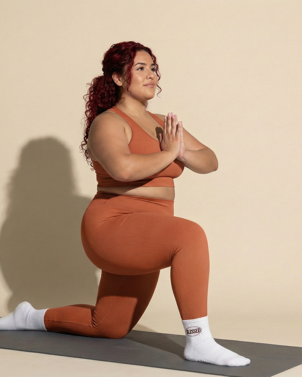 Person in brown athletic wear performing a yoga pose on a beige background