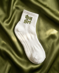 White grip sock with 'that girl' text on a green fabric background