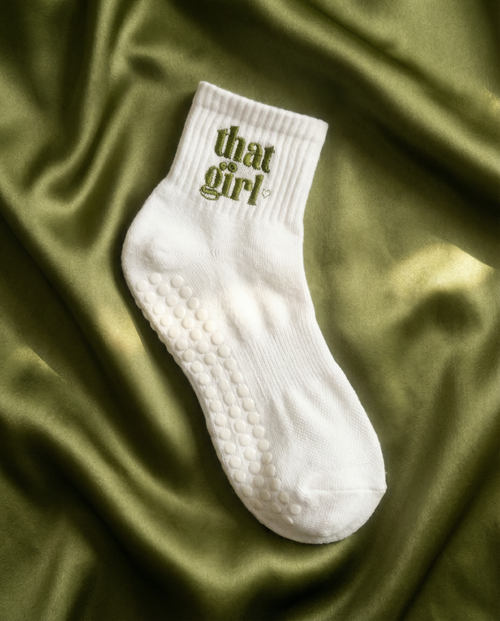 White grip sock with 'that girl' text on a green fabric background