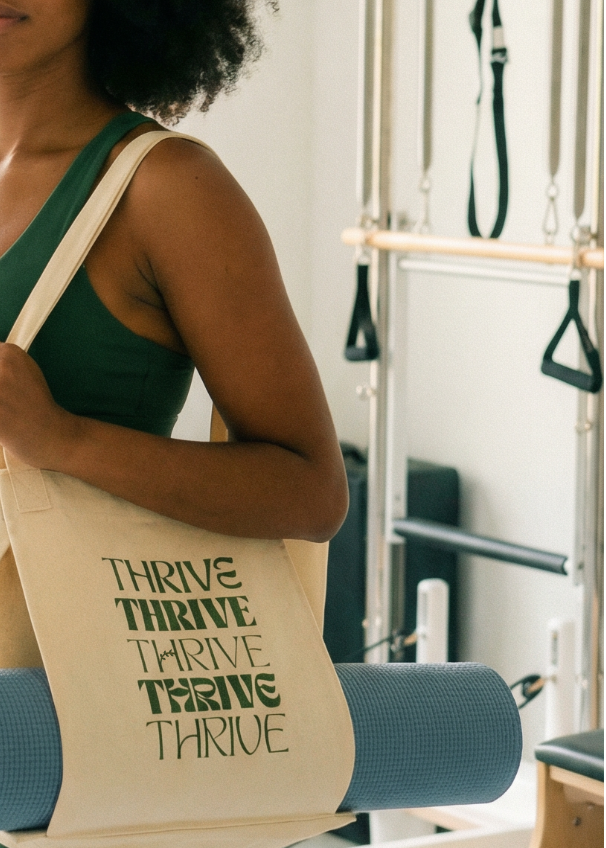 Person holding a beige tote bag with 'Thrive' text in a gym setting